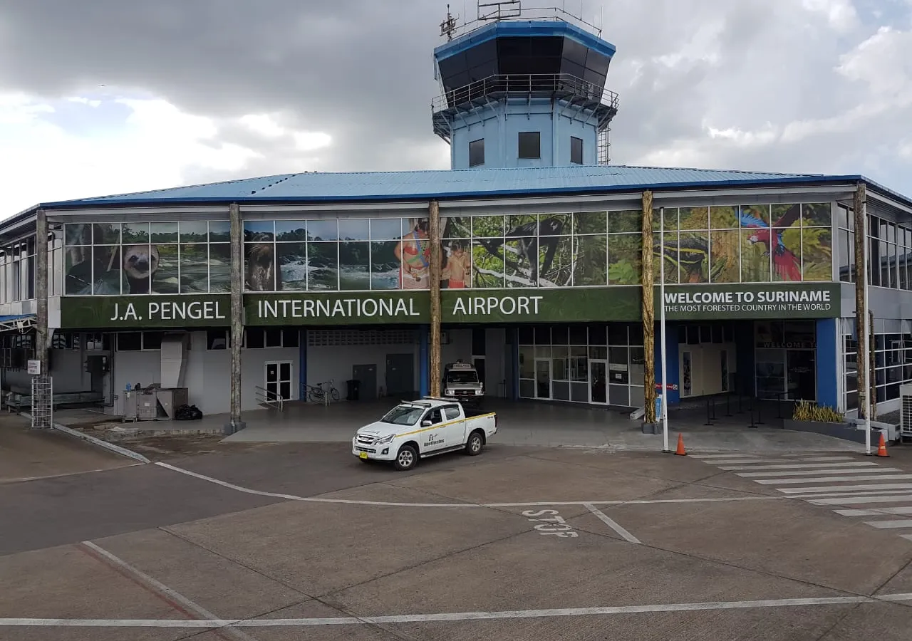 The front of J.A. Pengel International Airport, its upper windows covered with a band of Suriname nature photographs -- a sloth, rapids, a monkey, a macaw -- above the words "Welcome to Suriname, the most forested country in the world"
