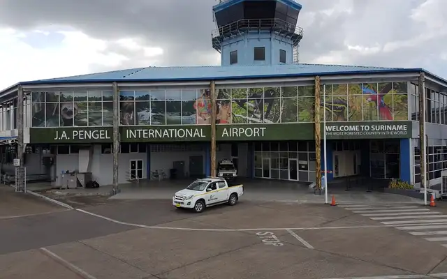 The front of J.A. Pengel International Airport, its upper windows covered with a band of Suriname nature photographs -- a sloth, rapids, a monkey, a macaw -- above the words "Welcome to Suriname, the most forested country in the world"