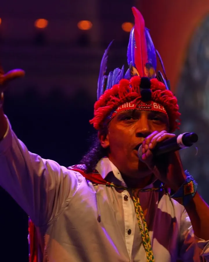 All Star Fresh performing on stage in a feathered headdress, microphone in hand