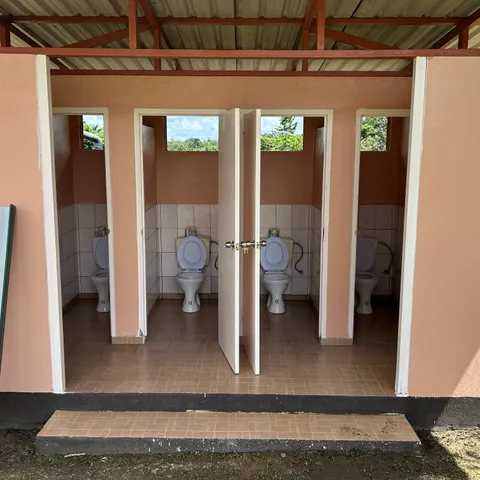 Four repaired toilet stalls in the tiled public bathroom beside the church, doors standing open