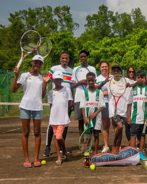 Jonge spelers van Community Tennis Suriname met hun coach op hun baan, met de rackets omhoog
