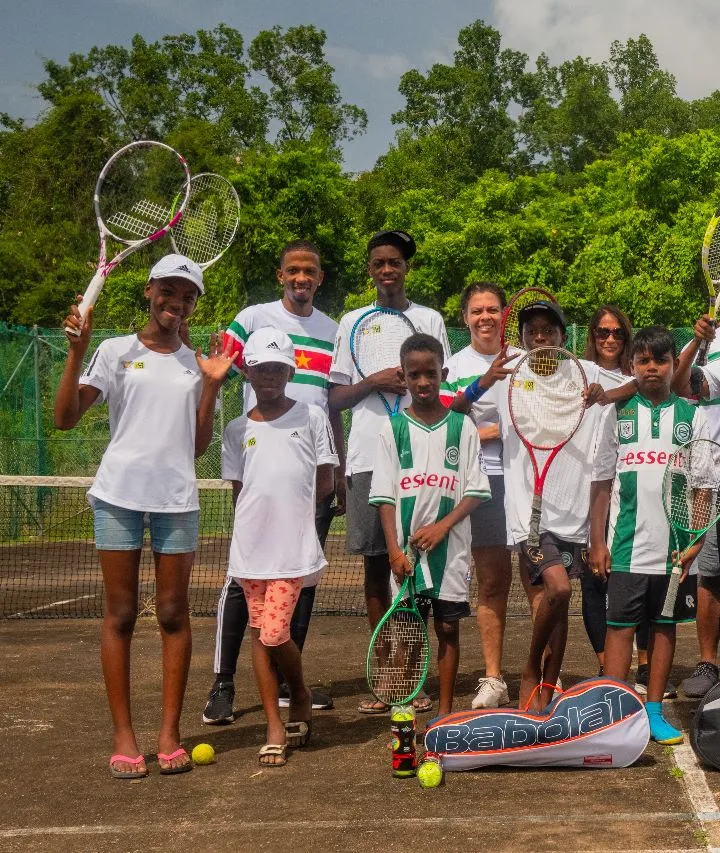 Young players of Community Tennis Suriname and their coach on their court, holding up their rackets