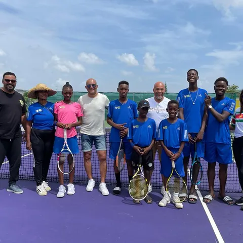 Young Community Tennis Suriname players in their blue kit, with their coaches and visitors, lined up along the net on the club's court with their rackets