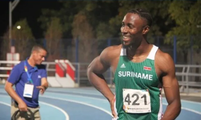 Danny Jeffrey Vanan smiling on an athletics track, wearing his Suriname racing vest