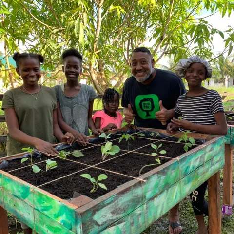 Children and a volunteer standing behind a painted garden table planted with seedlings