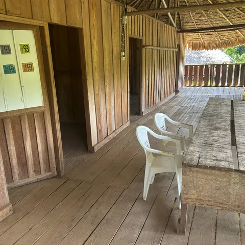 Inside the guesthouse: a timber-walled corridor opening onto a covered veranda under the thatch, with a cupboard carrying Forest93 stickers reading "for us", "for our future" and "for our children"