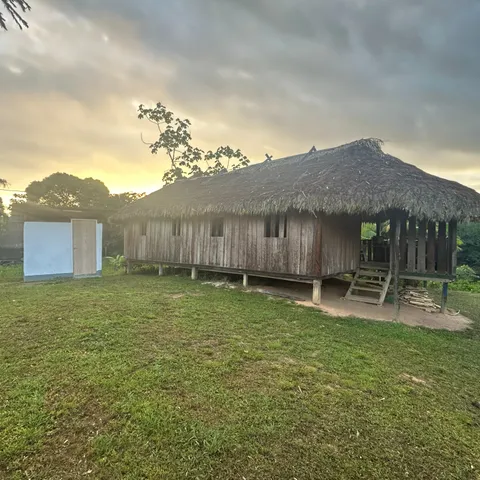 The guesthouse in Kwamalasamutu at dusk, a long building on stilts with a deep thatched roof and an open veranda at one end
