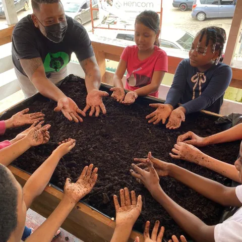 Children's hands spread out over fresh soil in a garden table