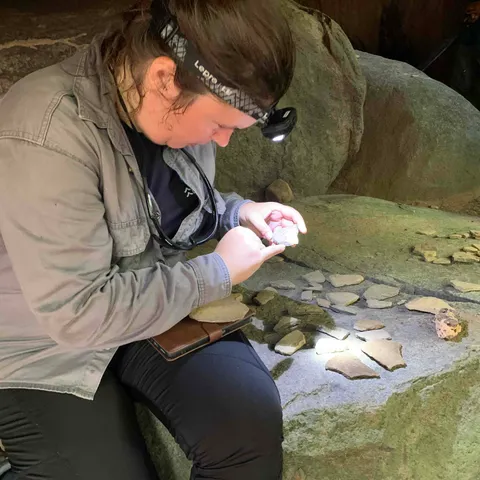 Irene Meulenberg, wearing a head torch, examines pottery fragments on a rock at Werehpai