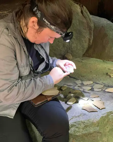 Irene Meulenberg, wearing a head torch, examines pottery fragments laid out on a rock at Werehpai