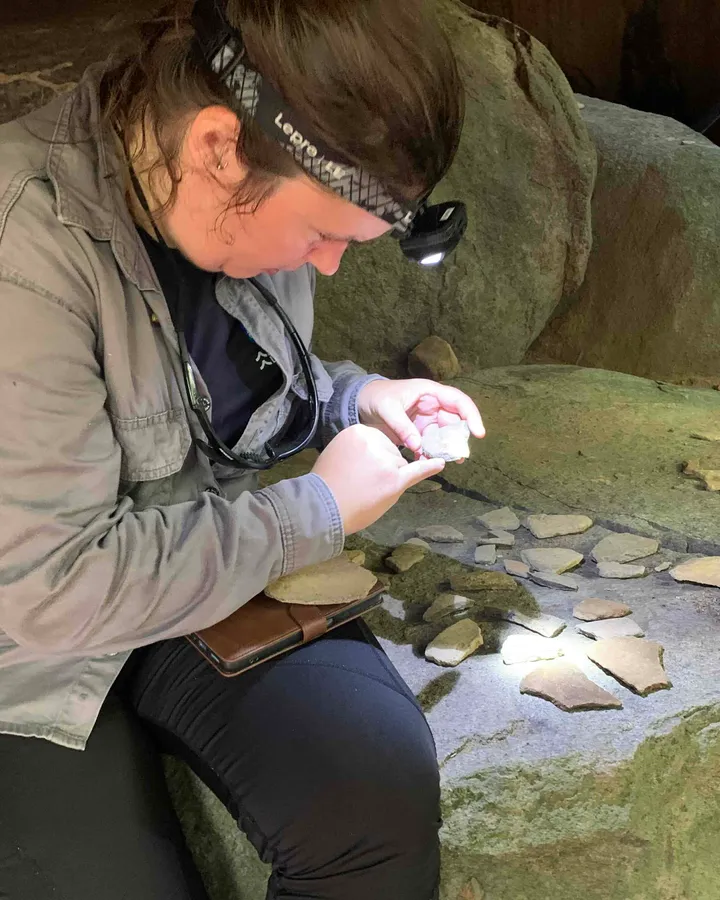 Irene Meulenberg, wearing a head torch, examines pottery fragments laid out on a rock at Werehpai