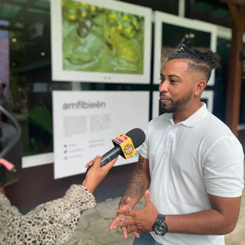 Jean-Pierre Veira being interviewed by a reporter in front of his exhibition, with framed wildlife photographs on the wall behind him