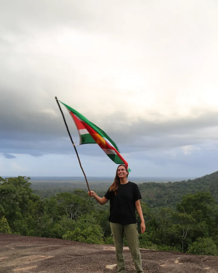 Lindsey van de Wetering waving the flag of Suriname on a granite outcrop high above the forest