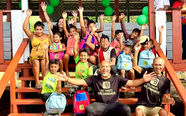 Kinderen van Amatopo met Forest93-schooltassen juichen op de trap van hun nieuwe school, met Dean Gorré tussen hen in en groene ballonnen aan de leuning