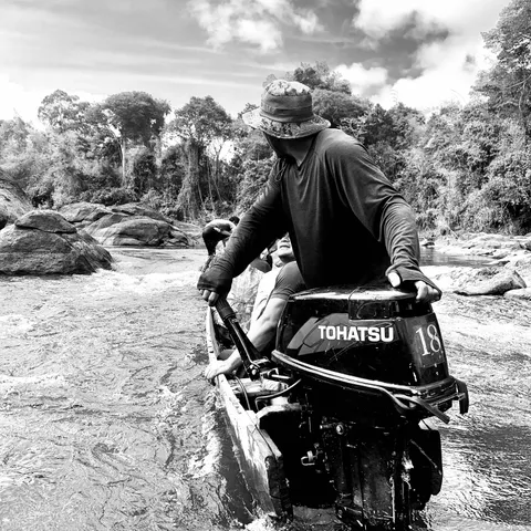 Black-and-white photo of a boatman steering an outboard motor through the rapids