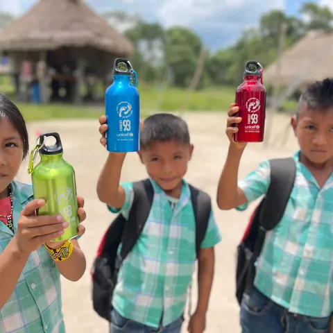 Three young schoolchildren proudly holding up reusable drinking bottles