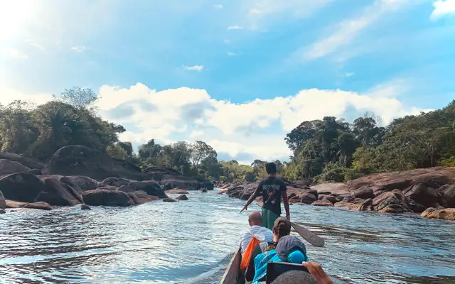 The group travelling upriver by boat between rocks, under a wide blue sky