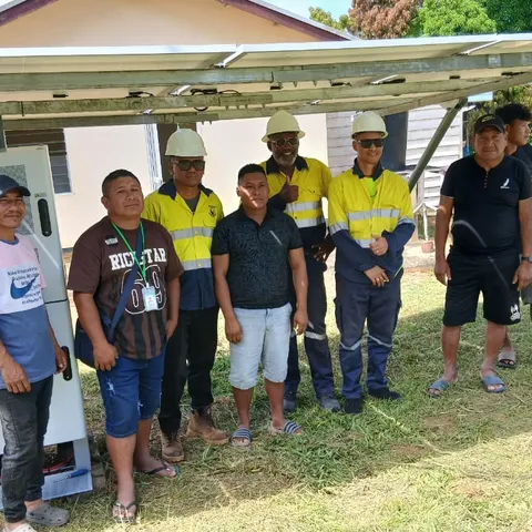 The Telesur crew and villagers standing under the new ground-mounted solar array beside its white inverter cabinet