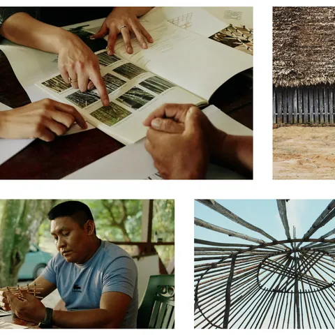 Hands turning the pages of the bamboo booklet showing photographed bamboo species, beside a thatched roof over a traditional split-wood wall and a bamboo roof structure seen from below