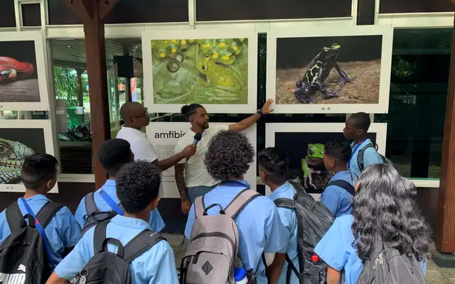 Jean-Pierre Veira pointing out a frog photograph to school students gathered in front of the amphibians panel of his exhibition