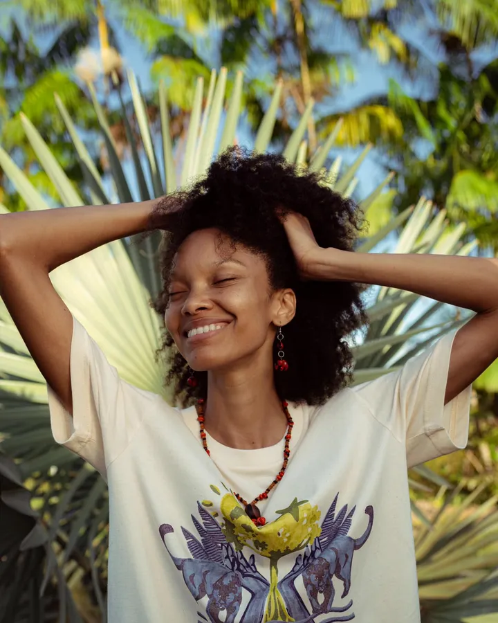 SuperSharda smiling with her hands in her hair, in front of palm leaves
