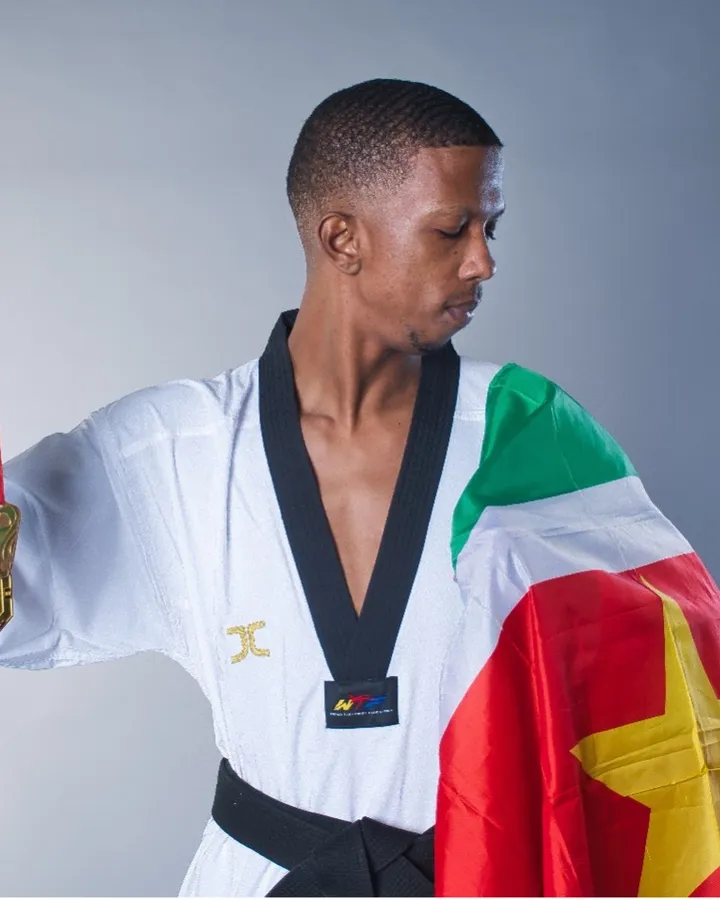 Tosh van Dijk in his taekwondo uniform, draped in the flag of Suriname, holding up his medals