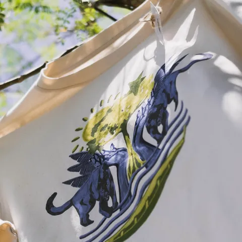 The front of the limited-edition t-shirt on a washing line, printed with Hedy Tjin's design of jaguars and birds around a stylised forest