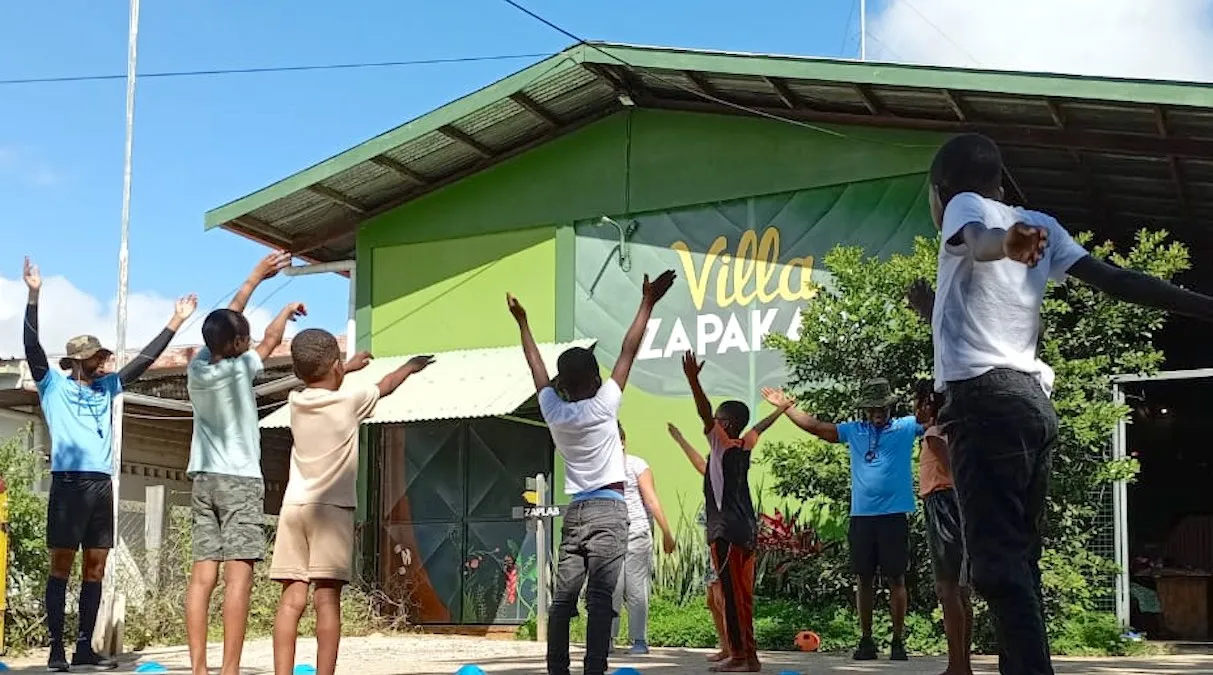 Children and their group leaders outside Villa Zapakara, arms stretched up towards the green gabled building with the museum's name painted on it (picture by Villa Zapakara)