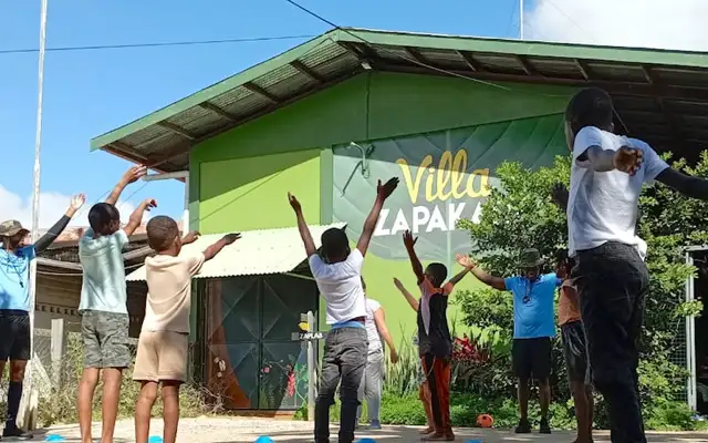 Children and their group leaders outside Villa Zapakara, arms stretched up towards the green gabled building with the museum's name painted on it (picture by Villa Zapakara)
