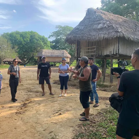 Visitors and villagers talking outside a thatched building in Kwamalasamutu